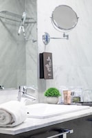 Un baño moderno con un lavabo de mármol blanco, un cabezal de ducha de mano, un espejo redondo y una pequeña planta en maceta.