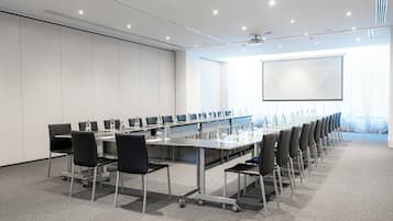 Een vergaderzaal met een lange tafel, stoelen, een projectiescherm en een whiteboard.