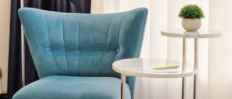 A blue armchair with a tufted backrest and wooden legs, positioned next to a small round table with a potted plant.