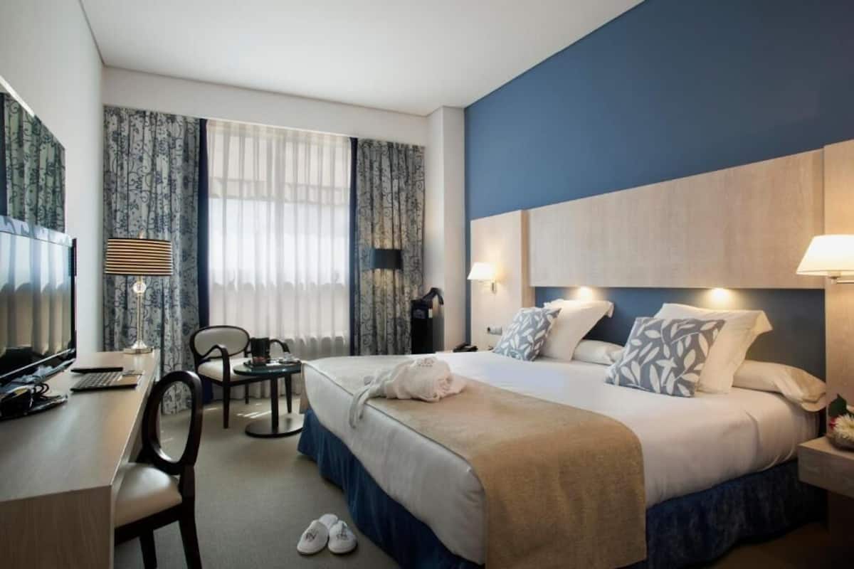 Habitación de hotel con cama, escritorio, silla y televisor.