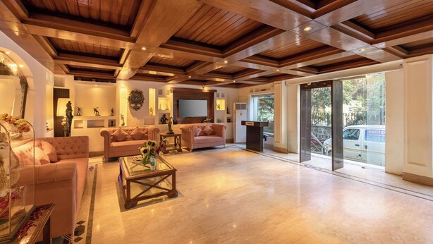 A spacious living room with a high ceiling and wooden beams, featuring a sofa, a coffee table, and a fireplace. - Hotel Emperor Palms at Karol Bagh (New Delhi)