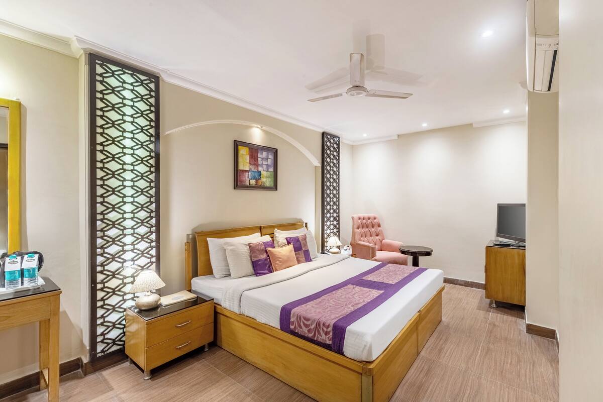 Una habitación de hotel moderna con una cama grande, un escritorio con lámpara, un televisor y un ventilador de techo.