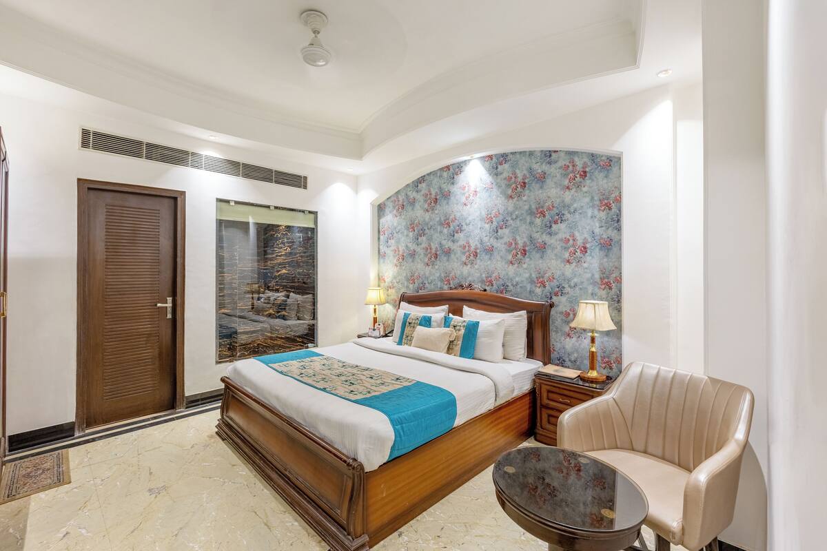 Un dormitorio con una cama grande, una silla, una mesita de noche y una pared curva con papel tapiz floral.
