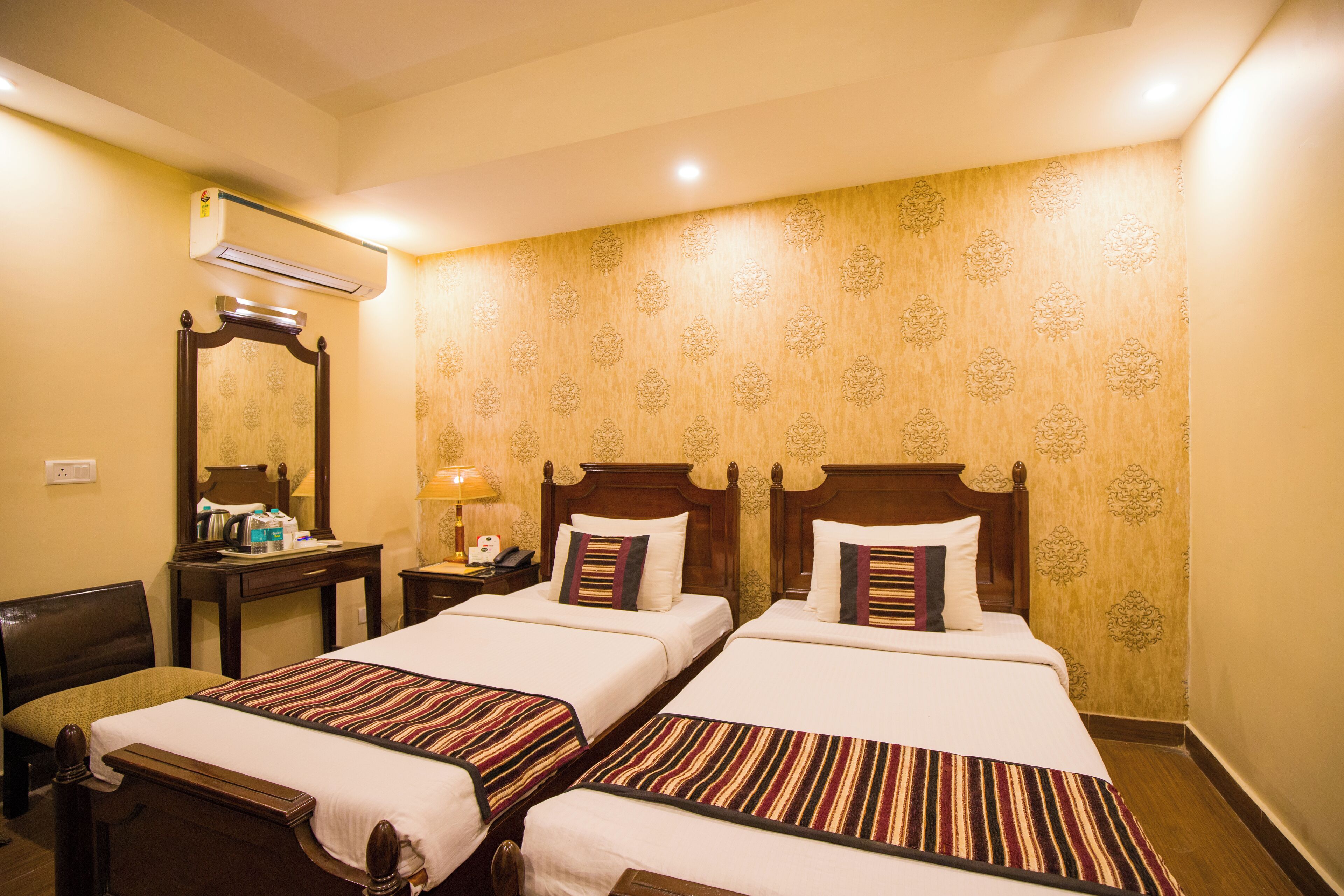 Quarto de hotel com duas camas, cabeceira de madeira, mesa de cabeceira, espelho e ar condicionado fixado na parede.