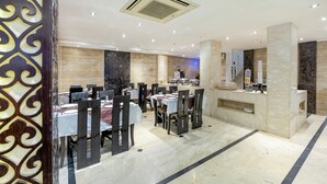 A modern restaurant with marble flooring, white tablecloths, and dark wooden chairs. - Hotel Emperor Palms at Karol Bagh (New Delhi)