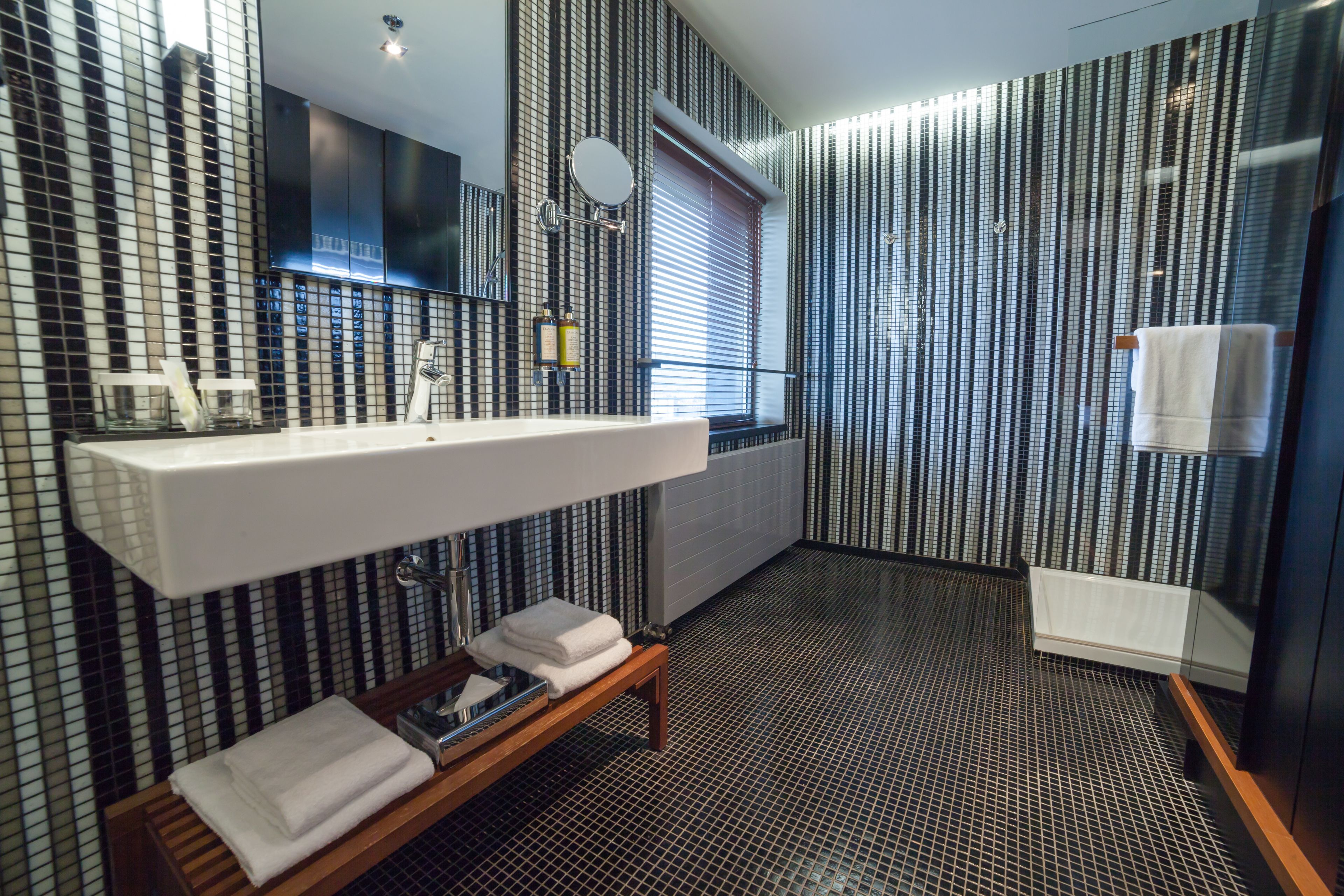 Un baño moderno con un espejo grande, un lavabo blanco y un banco de madera con toallas.