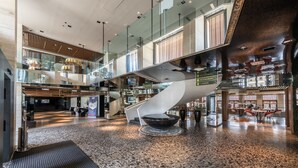 A spacious lobby with a central spiral staircase, a seating area with tables and chairs, and a bookstore in the background. - Hotel Yasmin (Kosice)