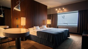 A hotel room with a bed, two bedside tables, a round table, and a view of the sky through the window. - Hotel Yasmin (Kosice)