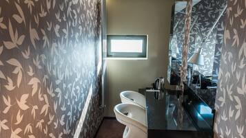 A bathroom with a modern design, featuring a black sink, white toilet, and a mirror with a leaf pattern.