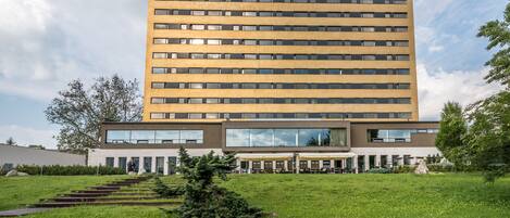 Un edificio de varios pisos con techo plano, ventanas grandes y un patio central con mesas al aire libre.