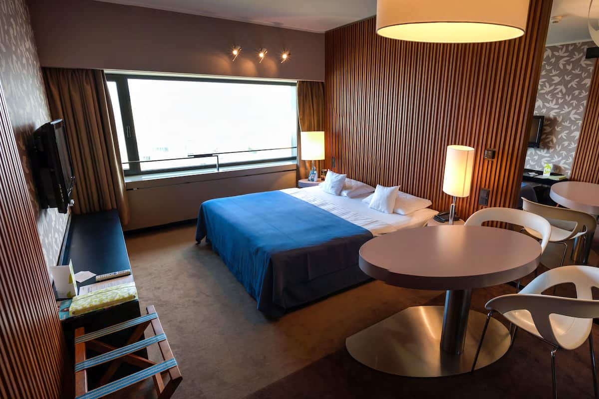 A hotel room with a large bed, a desk with a chair, a round table, and a TV mounted on the wall.