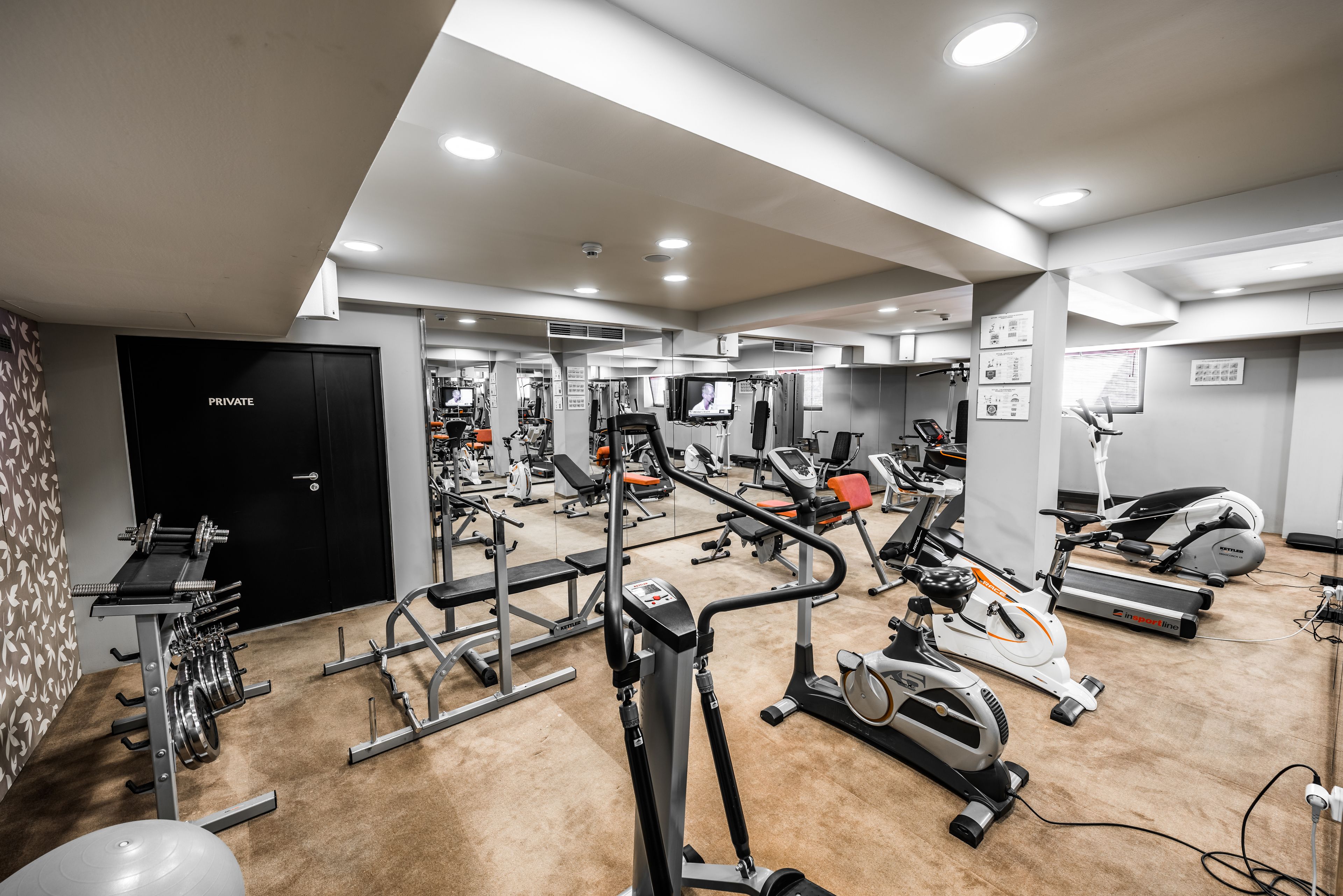 A gym with various exercise equipment, a private door, and a carpeted floor.
