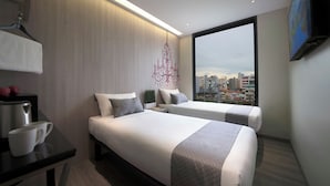 Una habitación de hotel moderna con dos camas, un escritorio y un amplio ventanal con vista a la ciudad.