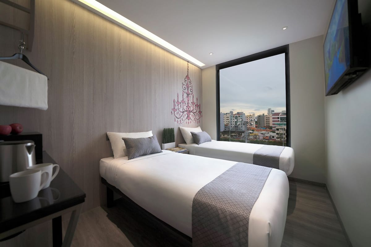 A modern hotel room with two beds, a desk, and a large window offering a city view.
