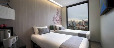 A modern hotel room with two beds, a desk, and a large window offering a city view.
