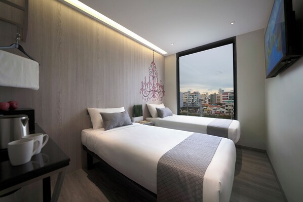 A modern hotel room with two beds, a desk, and a large window offering a city view.