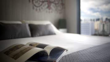 Un lit avec un livre dessus, un oreiller et une vue sur des immeubles par la fenêtre.