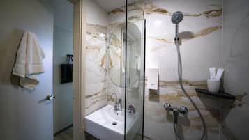 Un baño moderno con cabina de ducha de vidrio, un lavabo blanco y paredes de mármol.