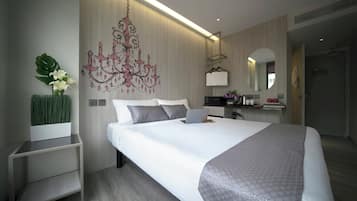 A modern hotel room with a large bed, bedside tables, a desk, a laptop, a chandelier, and a mirror.
