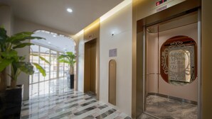 Un pasillo de hotel con suelo de mármol, plantas en macetas y un ascensor con un espejo decorativo.