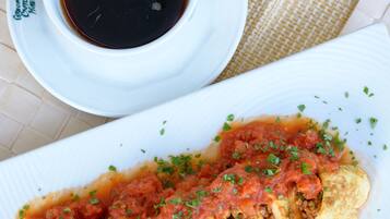 Un plato de pimientos rellenos con salsa y guarnición, una taza de café negro y un vaso de jugo de naranja sobre una mesa.