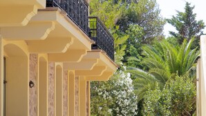 A yellow building with a balcony, stone pathway, and surrounding greenery. - Grecian Castle Hotel (Chios)