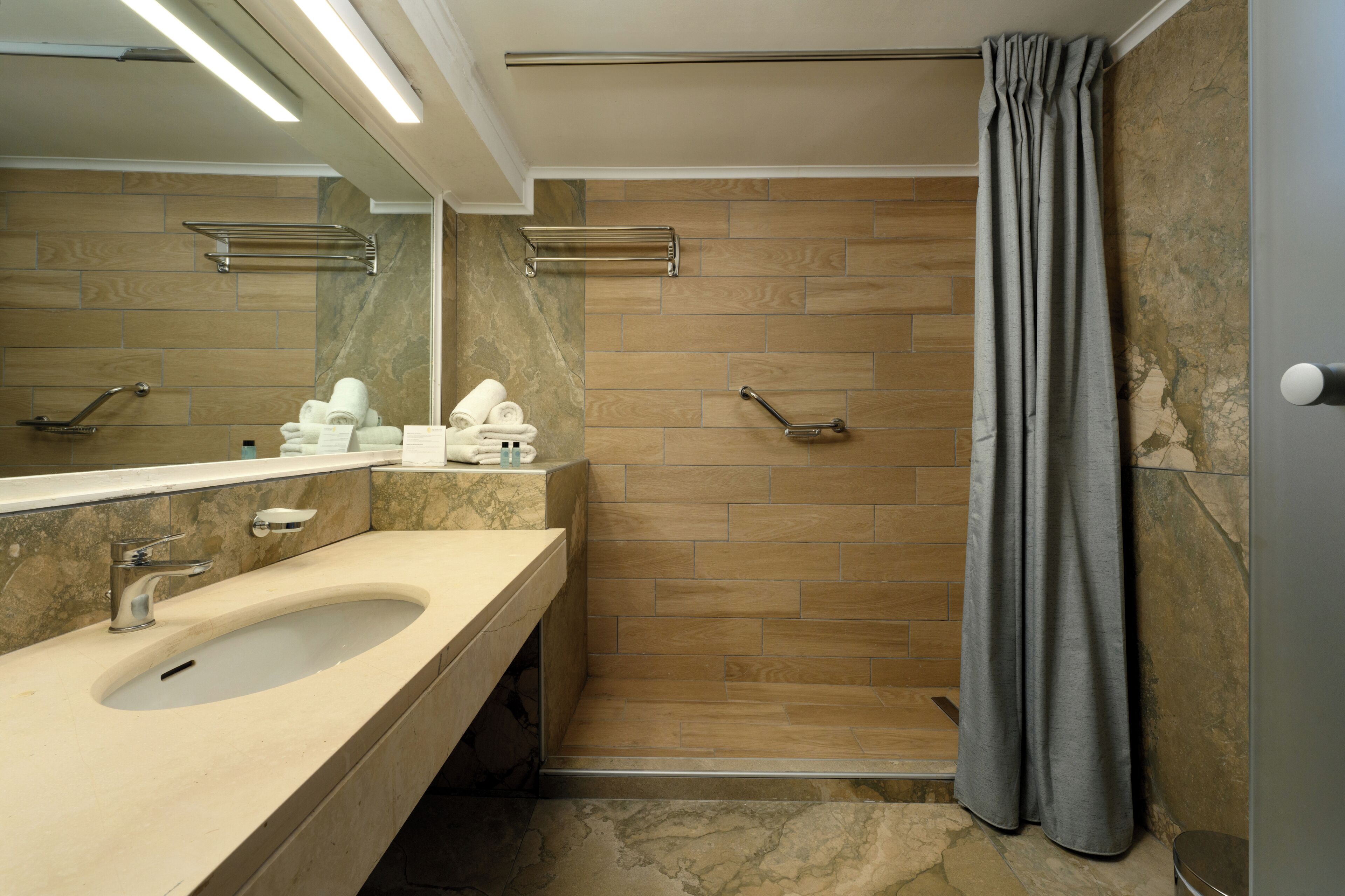 A modern bathroom with a large sink, a shower with a curtain, and a mirror above the sink.