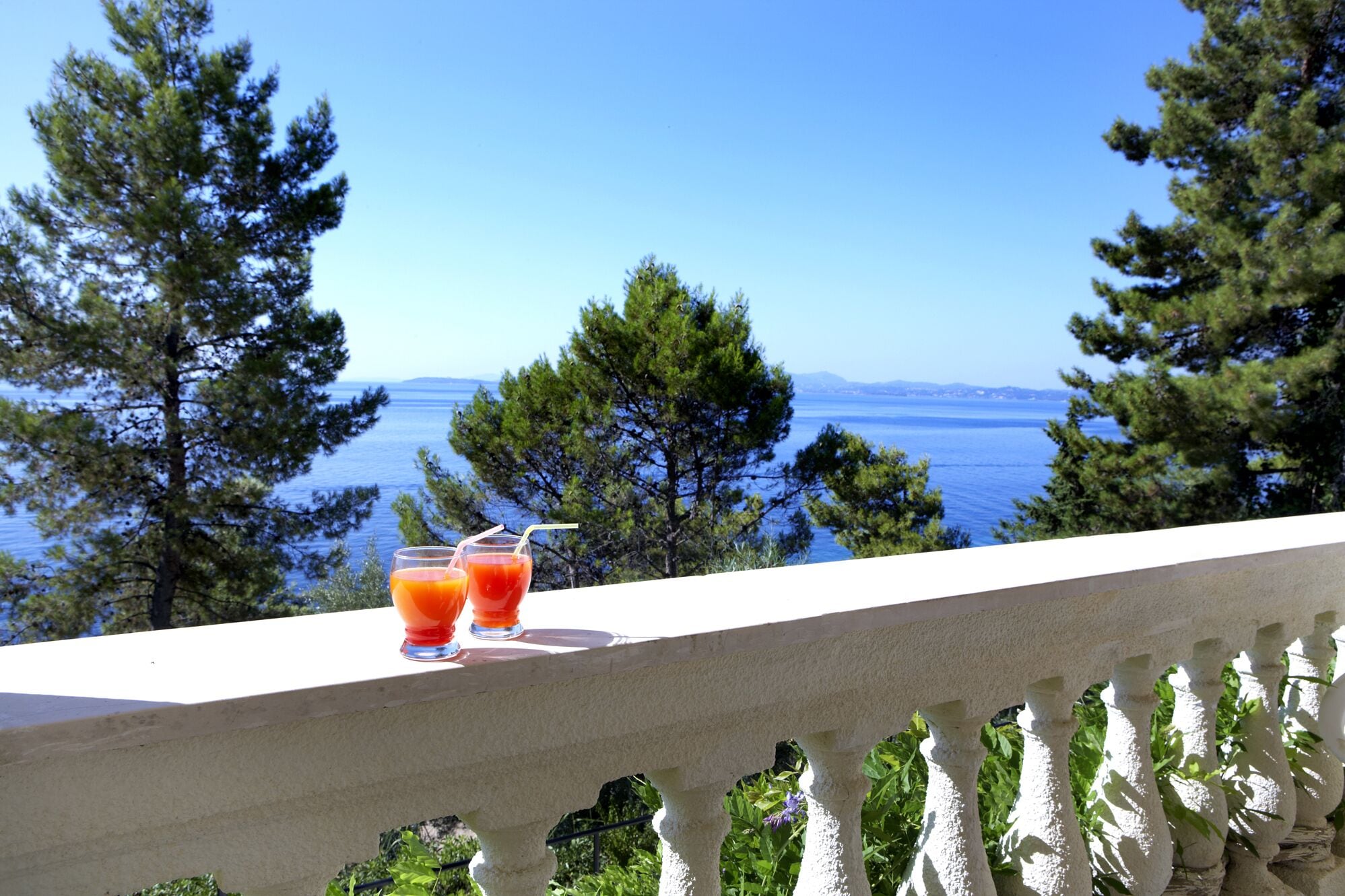 Een balkon met uitzicht op zee en bomen.