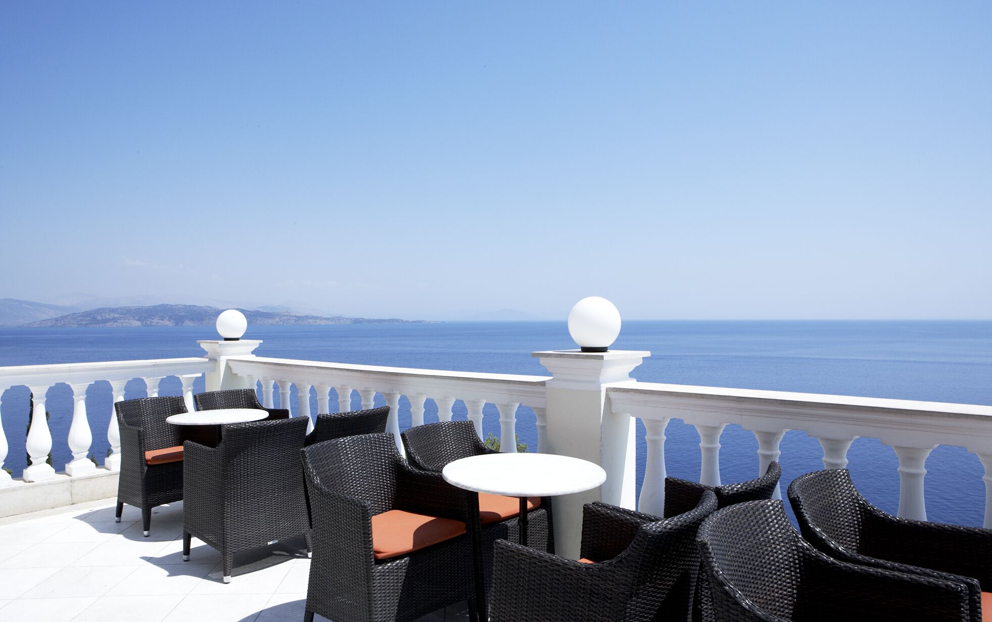 A terrace with wicker chairs and tables, overlooking a sea view.