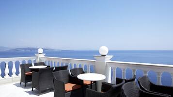 A terrace with wicker chairs and tables, overlooking a sea view.