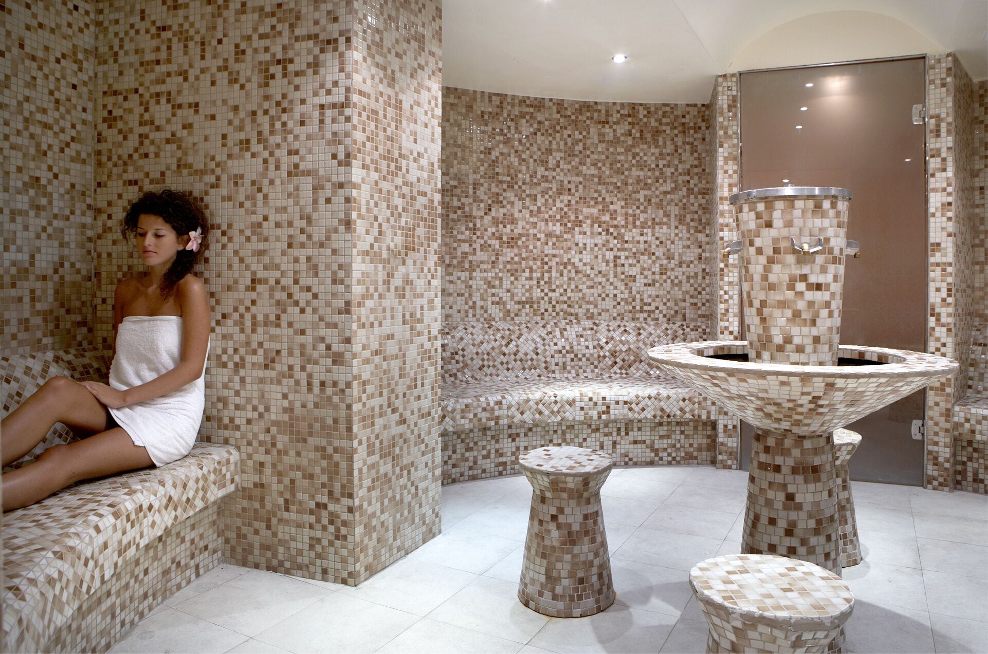 A spa area with mosaic tiled walls, a seating area, and a central water feature.