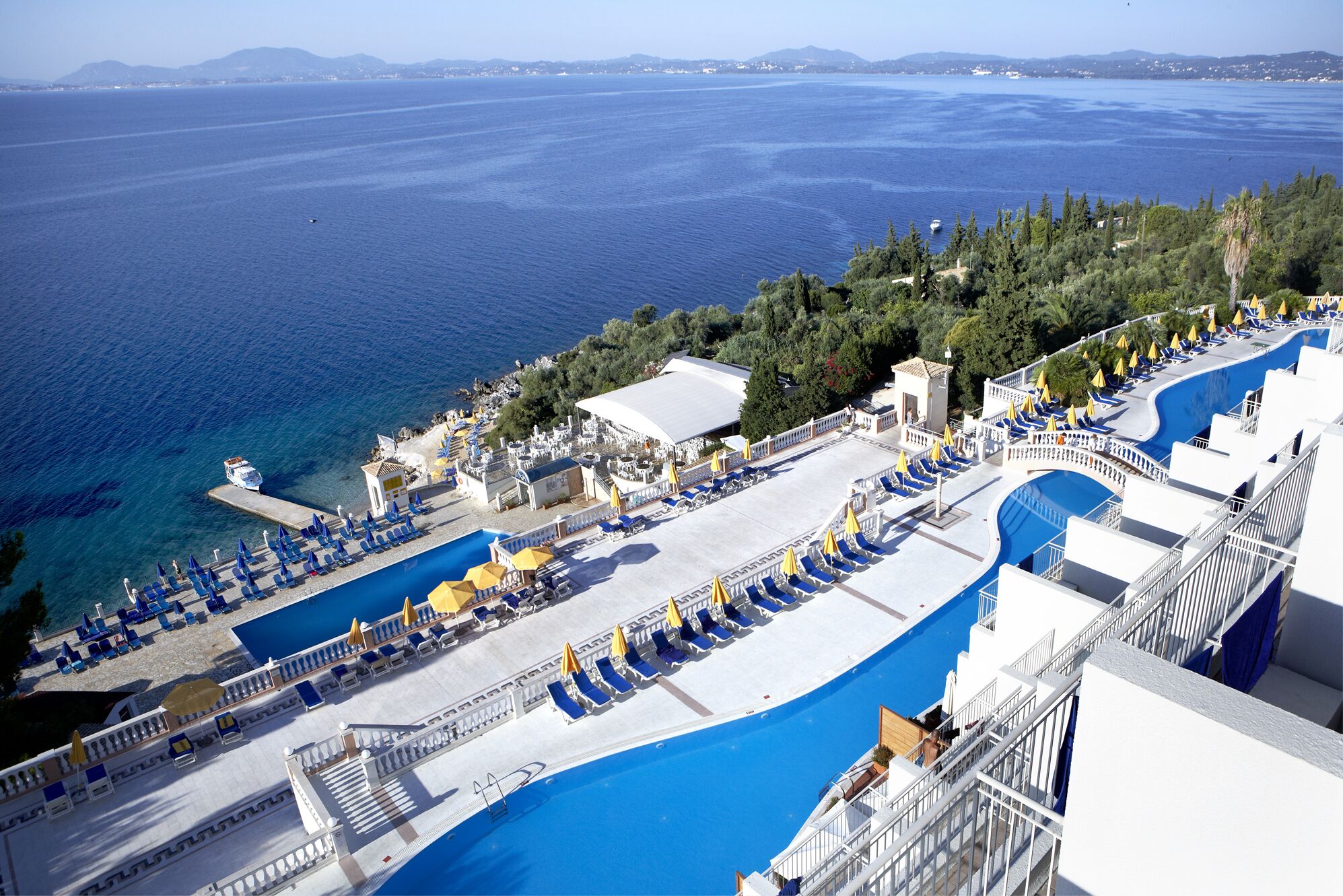 A resort with multiple swimming pools, sun loungers, and a view of the sea.