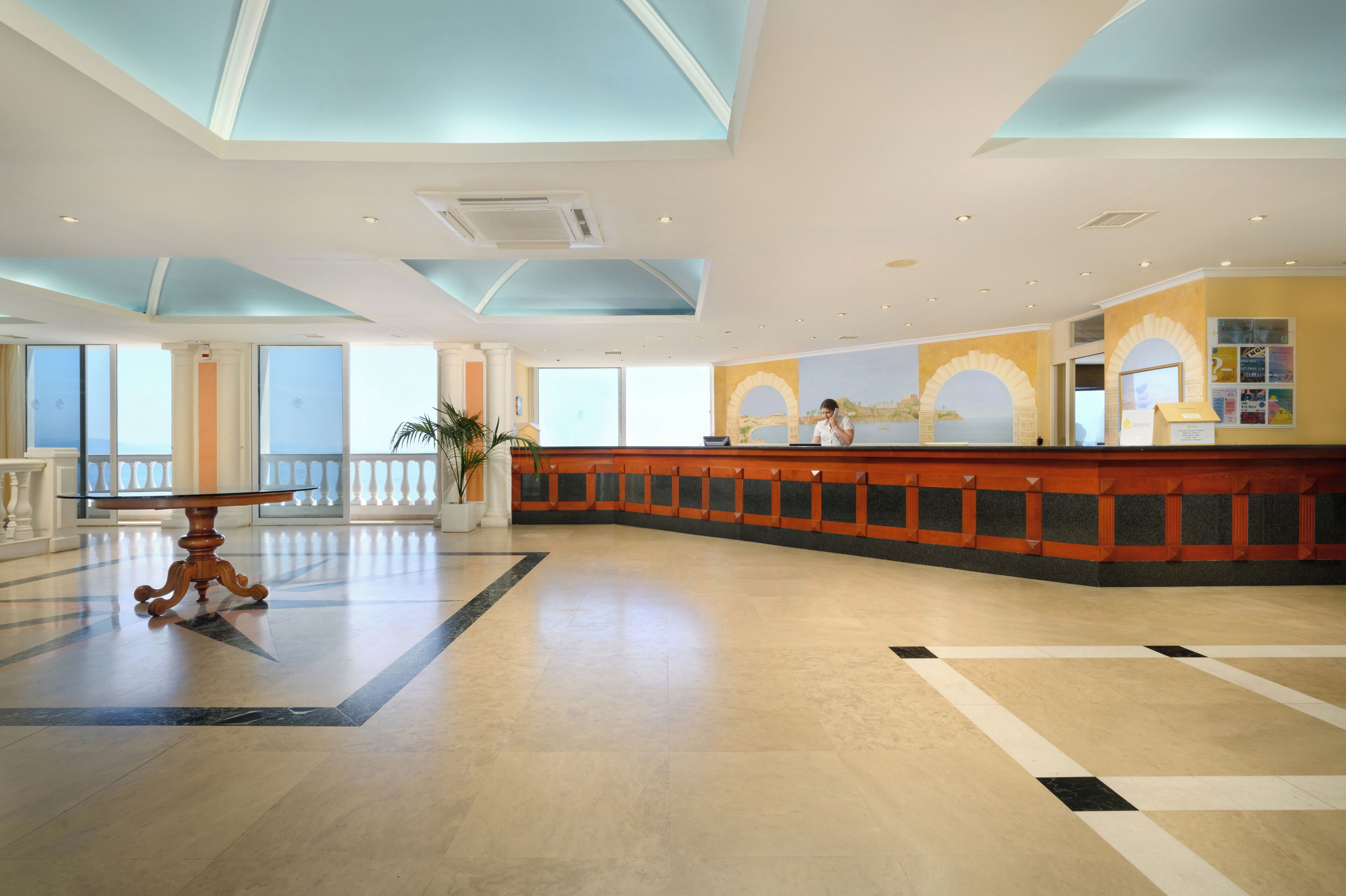 A spacious lobby with a reception desk, large windows, and a high ceiling.