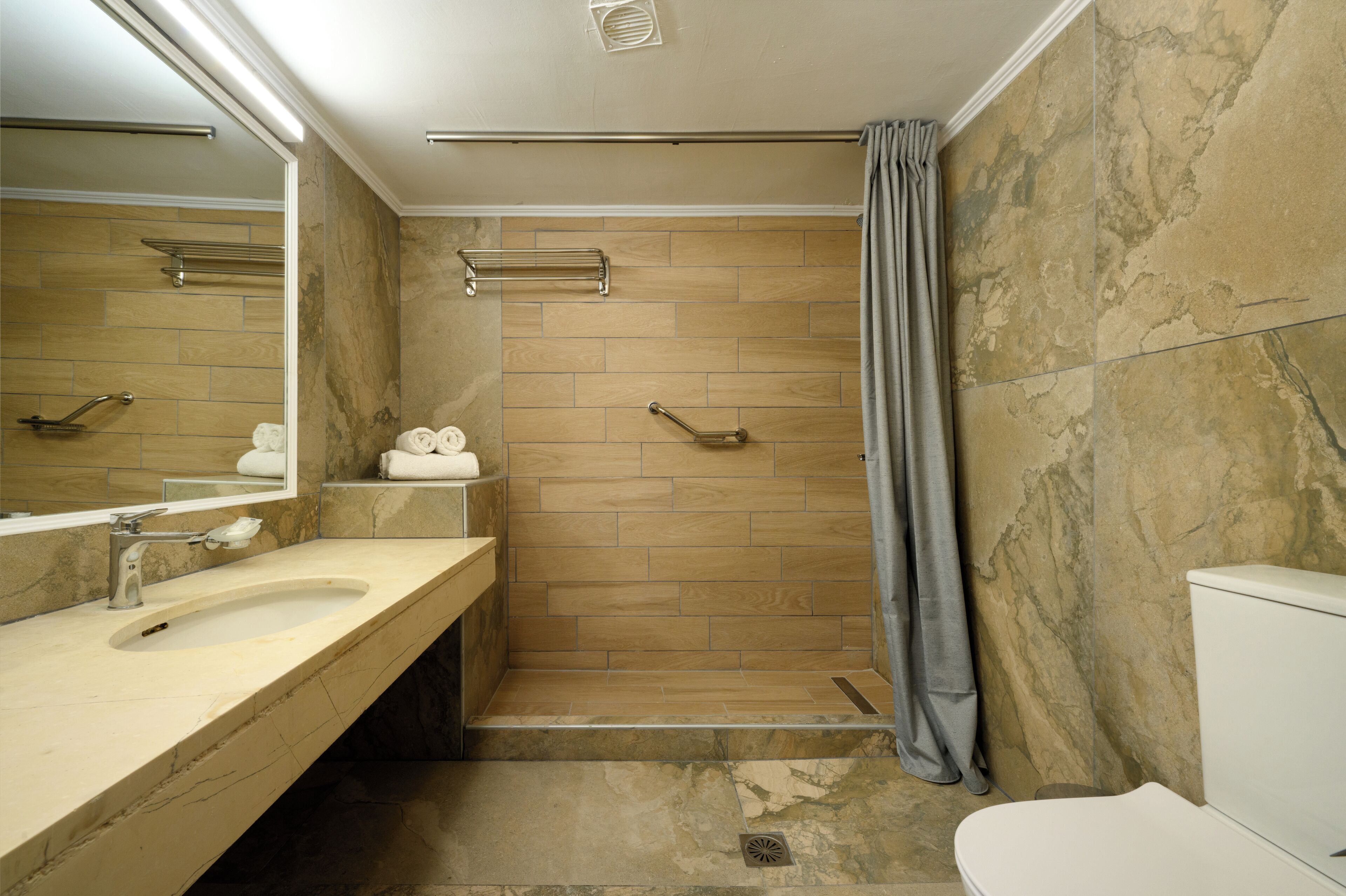A bathroom with a marble shower, a sink, and a toilet.