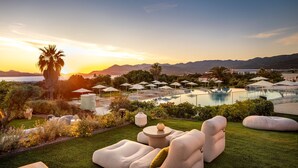 Zona junto a la piscina con sillones, sombrillas y vista al atardecer sobre las montañas.