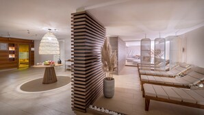 Un área de spa moderna con separadores de listones de madera, una mesa central de bambú con fruta y sillones de descanso.