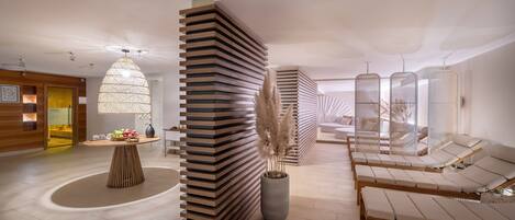 A modern spa area with wooden slat partitions, a central bamboo table with fruit, and lounge chairs.