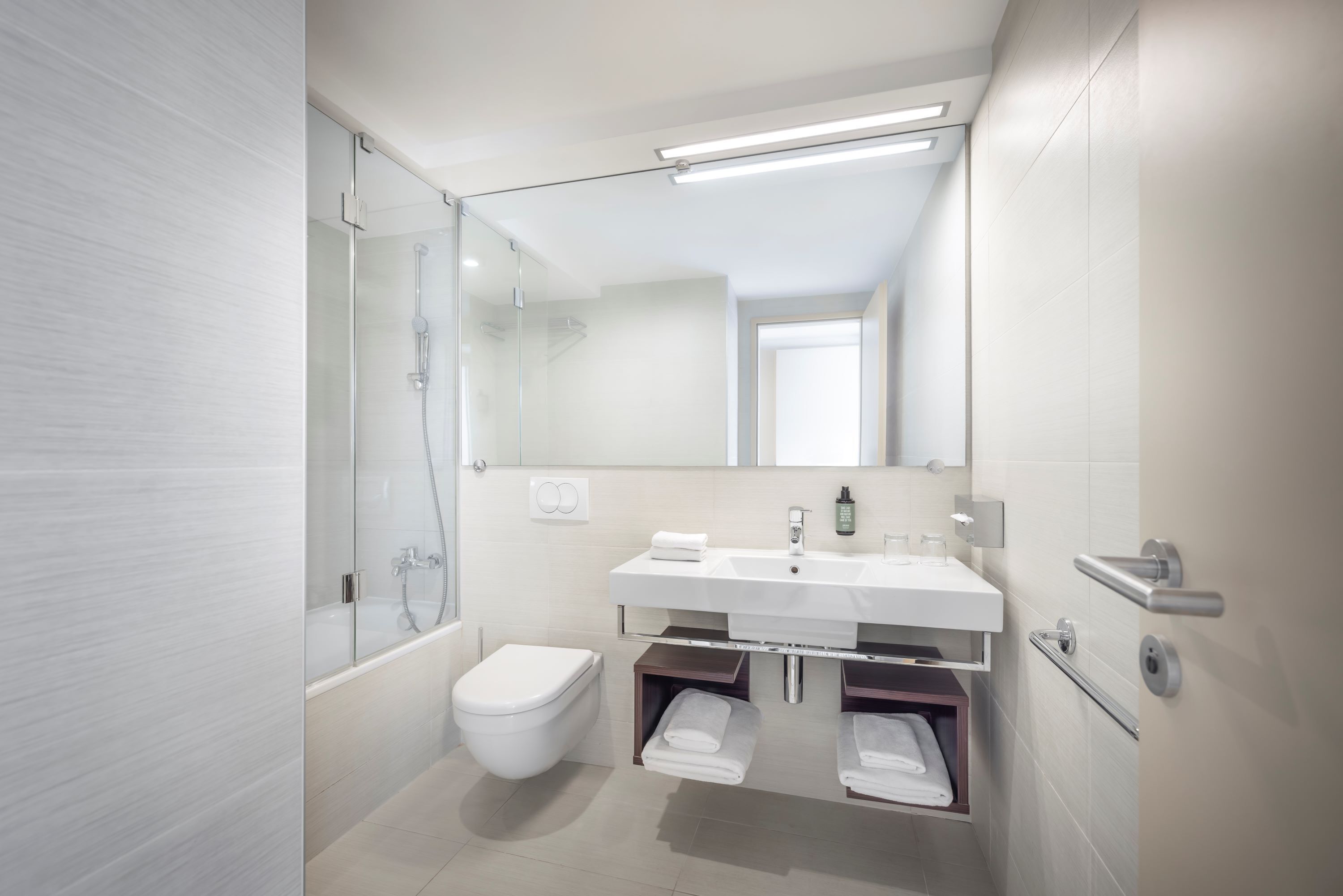 Un baño moderno con cabina de ducha de vidrio, inodoro y lavamanos blancos, y un perchero.