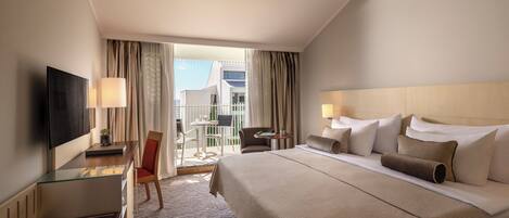 A hotel room with a bed, a desk, a TV, a chair, and a balcony with curtains.