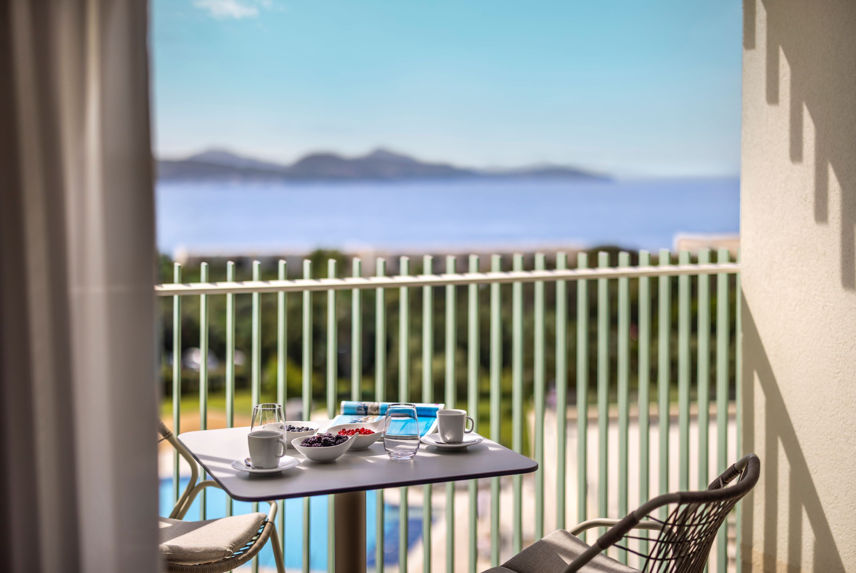 Un balcón con una mesa preparada para dos personas, con vistas a una masa de agua y tierras lejanas.
