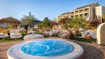 Área da piscina com hidromassagem, espreguiçadeiras e guarda-sóis.