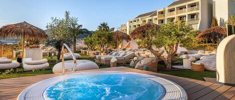 A pool area with a hot tub, lounge chairs, and umbrellas.