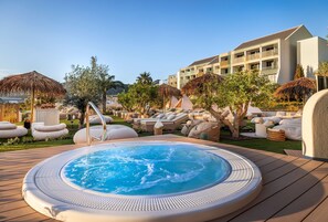 Área da piscina com hidromassagem, espreguiçadeiras e guarda-sóis.