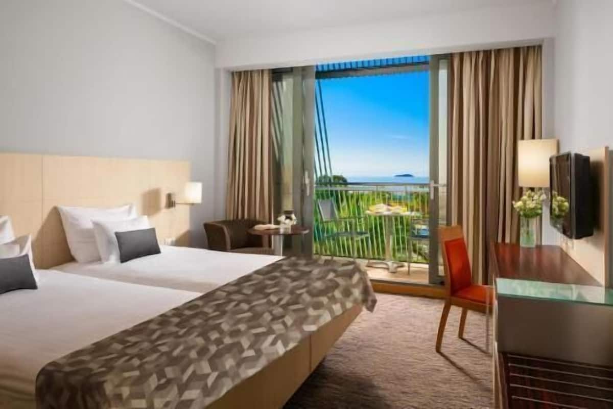 Habitación de hotel con dos camas, un escritorio, una silla, un televisor y un balcón con vistas.