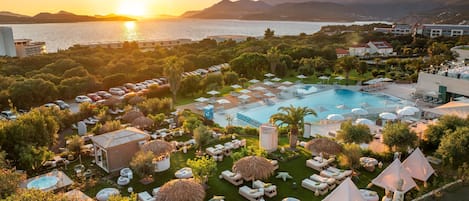 A resort with a large pool, lounge areas, and a view of the sea at sunset.