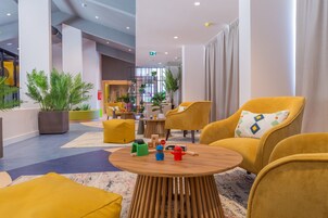 Um hall moderno com cadeiras amarelas, uma mesa de centro de madeira e plantas em vasos.