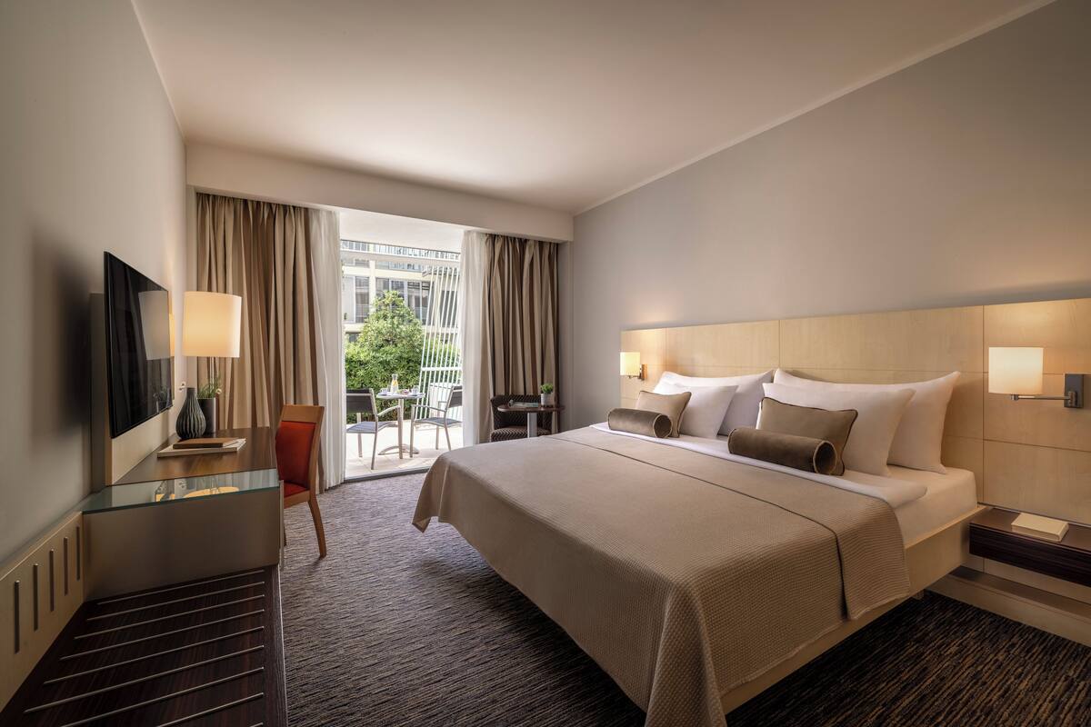 Habitación de hotel con una cama grande, un escritorio con una silla, un televisor y vistas al exterior.