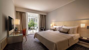 Quarto de hotel com uma cama grande, uma mesa com cadeira, uma TV e vista para o exterior.