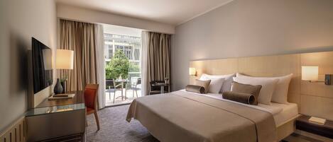 Habitación de hotel con una cama grande, un escritorio con una silla, un televisor y vistas al exterior.