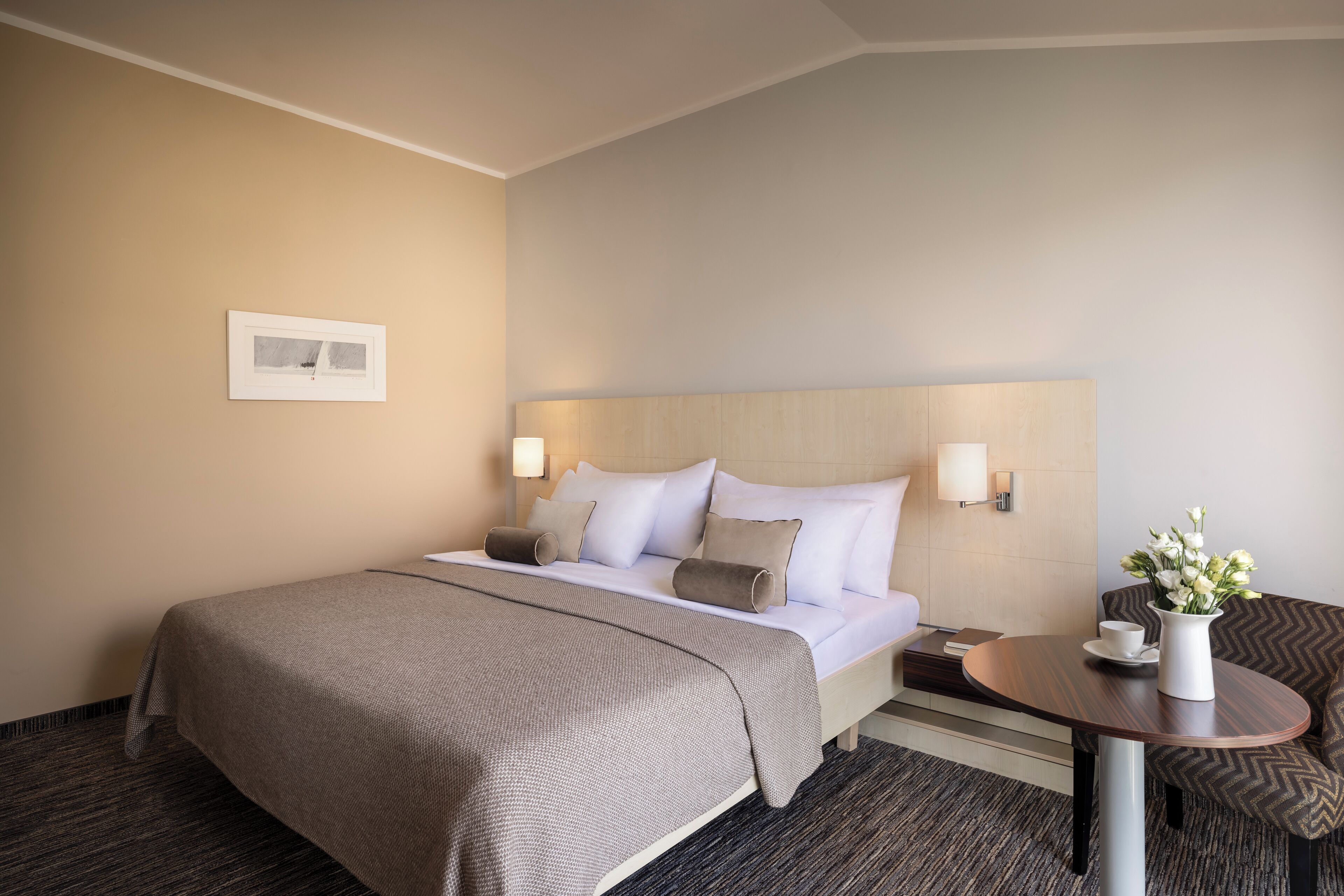 A hotel room with a bed, bedside tables, a small round table, and a chair.